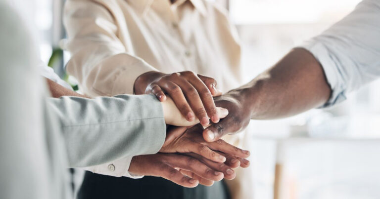 Close-up of diverse team members stacking hands together in a show of unity, teamwork, and collaboration in a professional setting.