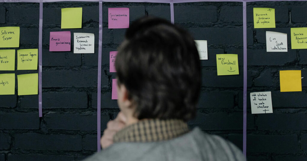 Person brainstorming in front of a wall with colorful sticky notes, symbolizing strategic planning and goal-setting, illustrating concepts from the blog post 'Is goal-setting just a bunch of hype?