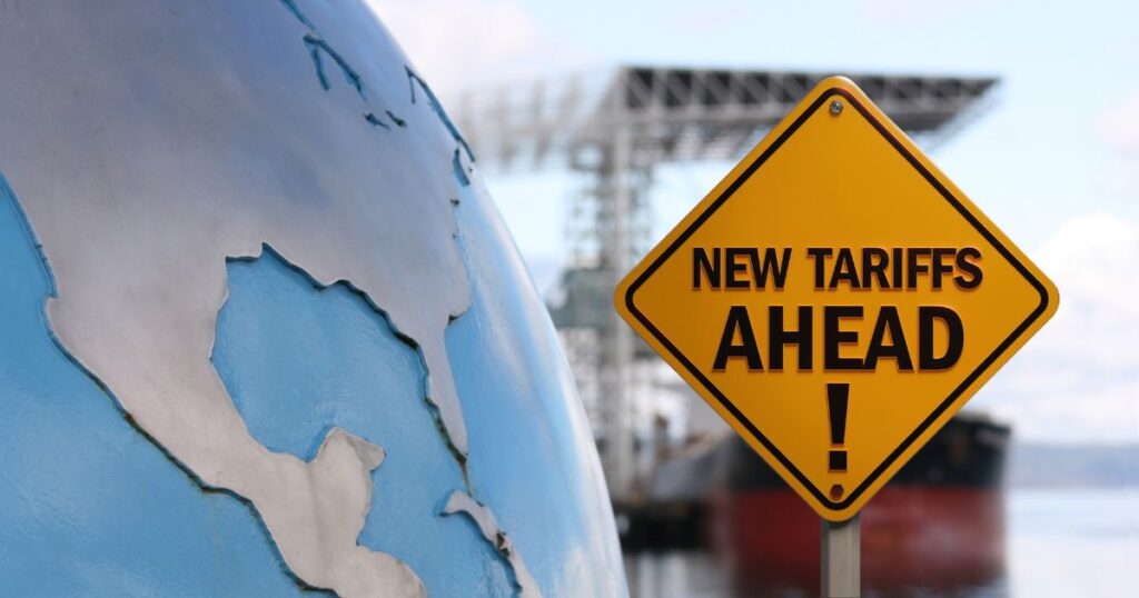 Yellow road sign reading "New Tariffs Ahead!" beside a globe showing North America, with a cargo ship and port in the background—symbolizing global trade impact.